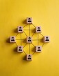 © Marko - Minimalist yellow background with black lines connecting people icons on wooden blocks