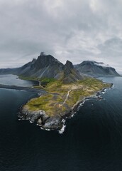 Wall Mural - Aerial view of a rugged coastal landscape with mountains and a cloudy sky.