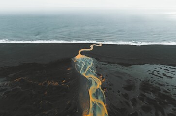 Poster - Aerial view of a winding river on a black sand beach.