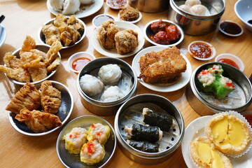 Traditional Chinese dim sum in metal bowl on wooden table. A lot of different kinds of food and drinks on the table