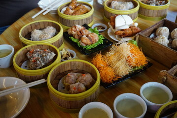 Traditional Chinese dim sum in metal bowl on wooden table. A lot of different kinds of food and drinks on the table