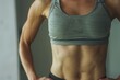 © Victor Bertrand - A fit woman in a grey sports bra stands confidently, emphasizing her muscular, toned abs and upper body strength.