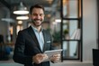 © Victor Bertrand - A young man in a tailored suit smiles confidently while holding a tablet in a modern office, emanating professionalism and enthusiasm.
