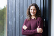 © Wavebreak Media - Smiling woman with curly hair standing with arms crossed, wearing maroon sweater, copy space
