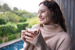 © Wavebreak Media - Smiling woman holding cup of tea, relaxing at home with scenic view