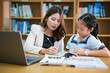 © EduLife Photos - Teacher Helping Young Student with Schoolwork in Library. A teacher guides a young student with schoolwork in a library setting, focusing on personalized learning and academic development.