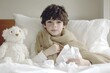 © AI Farm - A young boy bundled in a blanket, resting in bed with a teddy bear and tissues, conveying a feeling of warmth and comfort.