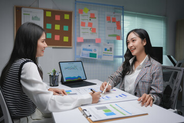 Two businesswomen are discussing financial charts at a meeting in a modern office, smiling and collaborating on a project