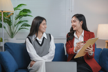 Wall Mural - Two young businesswomen smiling and looking at each other while having a productive business meeting on the sofa