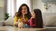 © Yuliia - Caucasian family laughing woman female mother mom with little girl happy schoolgirl kid preschool smiling daughter counts puts coins piggy bank parent child save money financial literacy indoors home