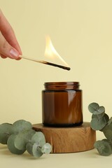 Poster - Woman lighting candle on pale yellow background, closeup