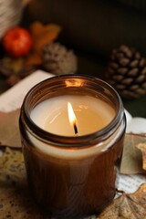 Poster - Burning candle and dry leaves on blurred background, closeup. Autumn atmosphere