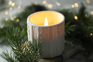 Sticker - Burning candle, fir tree branches on table against blurred lights, closeup