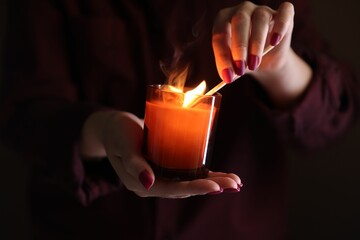 Sticker - Woman lighting candle with match in darkness, closeup