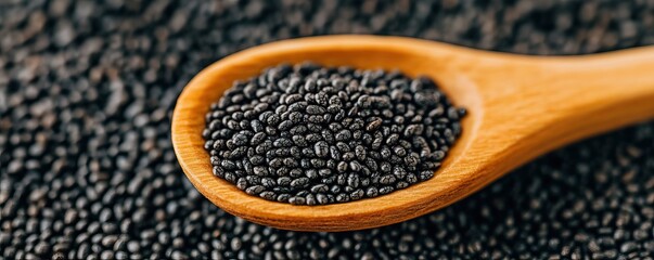 A close-up view of black sesame seeds in a wooden spoon, surrounded by a scattering of more seeds, showcasing their rich texture and color.