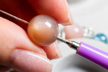 Close up of young Caucasian woman's hands assembling a bracelet of stone beads and precious metals in her workshop. Exclusive custom jewelry