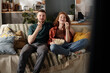 © pressmaster - Happy young woman laughing and eating popcorn while sitting next to her puzzled boyfriend looking at tv screen