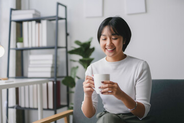 Young woman is sitting on her sofa at home, enjoying a quiet moment with a cup of coffee