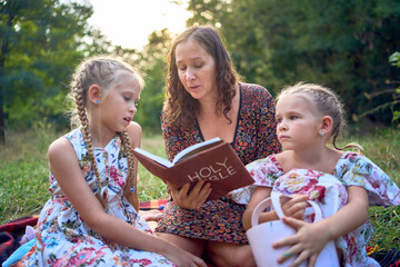 Wall Mural - a mother and her two daughters read the holy bible and pray at an Easter picnic