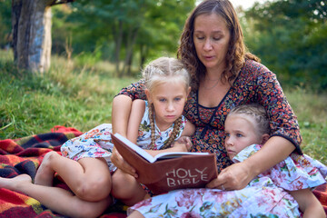 Wall Mural - a mother and her two daughters read the holy bible and pray at an Easter picnic