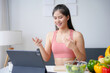 © amnaj - Smiling asian nutritionist in sportswear talking on a video call about healthy food, giving online fitness and diet advice