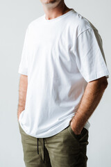 A casual portrait featuring a man wearing a simple white tshirt paired with olive green pants, all set against a light and neutral background