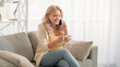 © golubovy - Happy maternity. Excited woman. Mobile news. Cheerful lady holding pregnancy test talking smartphone expressing joy sitting sofa light room interior.