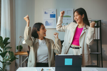 Wall Mural - Two young businesswomen are celebrating a success raising their arms in a luminous office