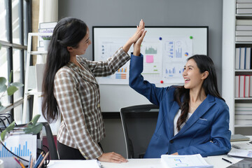 Wall Mural - Two happy businesswomen are giving each other a high five in the office, celebrating achieving business goals