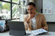 © amnaj - Businessman is reviewing financial reports and using a tablet for a video conference in the office