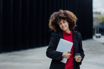 Wall Mural - young African American business woman using laptop or computer in city of Latin America, Hispanic financial and caribbean people with afro hair and skyscraper background	