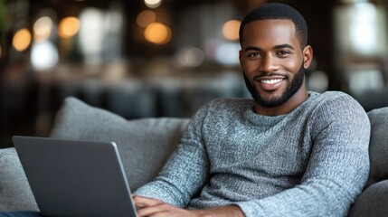 A cheerful young man is using his laptop on a comfortable couch in a lively cafe setting