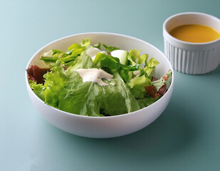 Fresh salad in a white bowl with dressing on the side isolated on a minimalist background