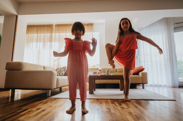 Two young girls in red dresses enjoy dancing playfully in a sunny and cozy living room setting, capturing joy and childhood fun.