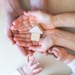 © Michael - A child's hand holds a key and reaches for a small wooden house that lies in the open hands of its parents.