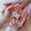 © Michael - A child hand reaches for a small wooden toy house in the open hands of his parents.