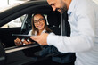 © Zamrznuti tonovi - Woman in car talking with man holding tablet outside vehicle in a car showroom
