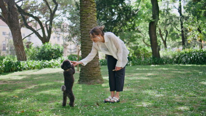 Happy woman playing poodle on green park grass. Girl with furry black puppy