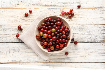 Bowl with fresh gooseberries on white wooden background