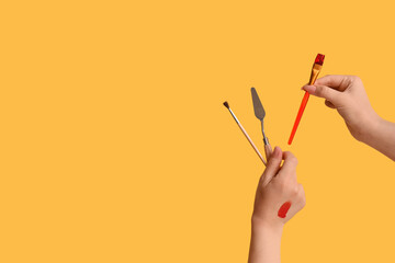 Wall Mural - Female hands with artist's brushes and palette knife on yellow background