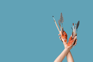 Wall Mural - Female hands with artist's brushes and palette knives on blue background