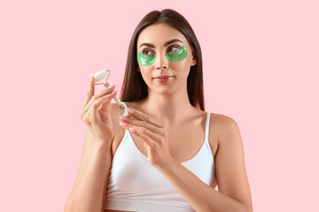 Wall Mural - Pretty young woman with under-eye patches and face massage roller on pink background