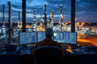 © Prasanth - An engineer oversees refinery operations from a control room workstation as evening light illuminates the facility's machinery and infrastructure