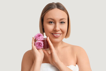 Canvas Print - Beautiful mature woman with bottle of essential oil and flowers on light background, closeup