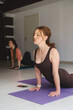 © ninelutsk - Yoga teacher demonstrates pose as students follow along in light studio. Group practice on morning session with mid aged woman class