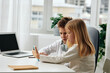 © SHOTPRIME STUDIO - Happy Caucasian boy and girl studying together at home They are sitting at a table, fully engaged in elearning using laptops, tablets, and phones The siblings are wearing headphones, displaying
