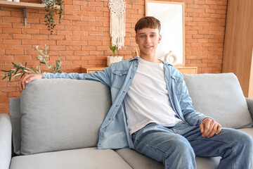 Sticker - Young man sitting on grey sofa at home