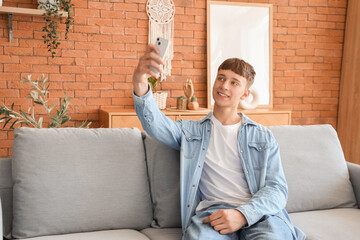 Poster - Young man with mobile phone taking selfie on grey sofa at home