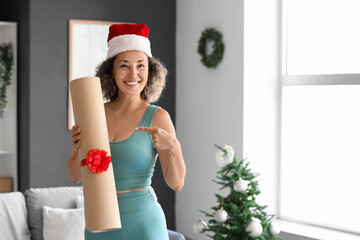 Canvas Print - Sporty mature woman in Santa hat with gift yoga mat at home on Christmas eve