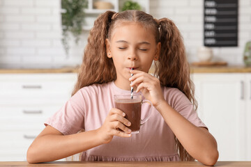 Wall Mural - Cute girl drinking sweet hot cocoa at table in kitchen